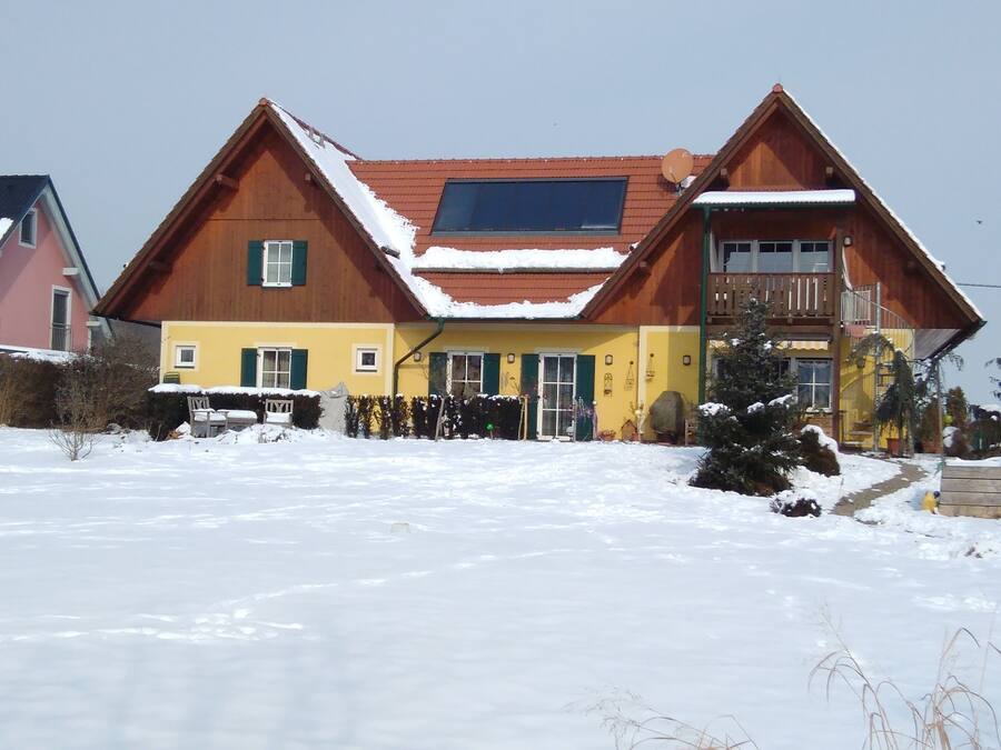 A two-story wooden house with a sloped roof, a balcony, and a large window.