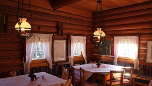 Eine rustikale Holzhütte mit mehreren Esstischen und Stühlen, dekoriert mit weißen Tischdecken und Pendelleuchten.