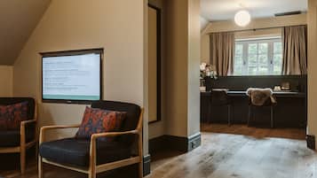 Una habitación acogedora con piso de madera, un ventanal con cortinas, un escritorio y una silla con cojín.