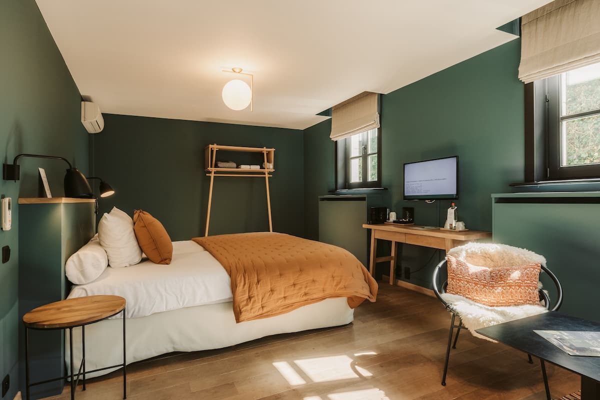 A bedroom with a bed, a desk, a chair, a TV, and a window.