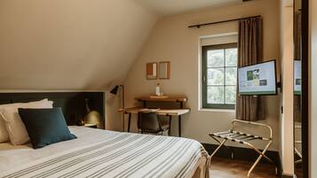 Une chambre à coucher avec un lit, un bureau et une chaise. Il y a une fenêtre avec des rideaux et un téléviseur fixé au mur.