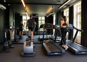 A gym with treadmills, ellipticals, and a stationary bike, large windows, and a dark interior. - Auberge du Pêcheur (Sint-Martens-Latem)