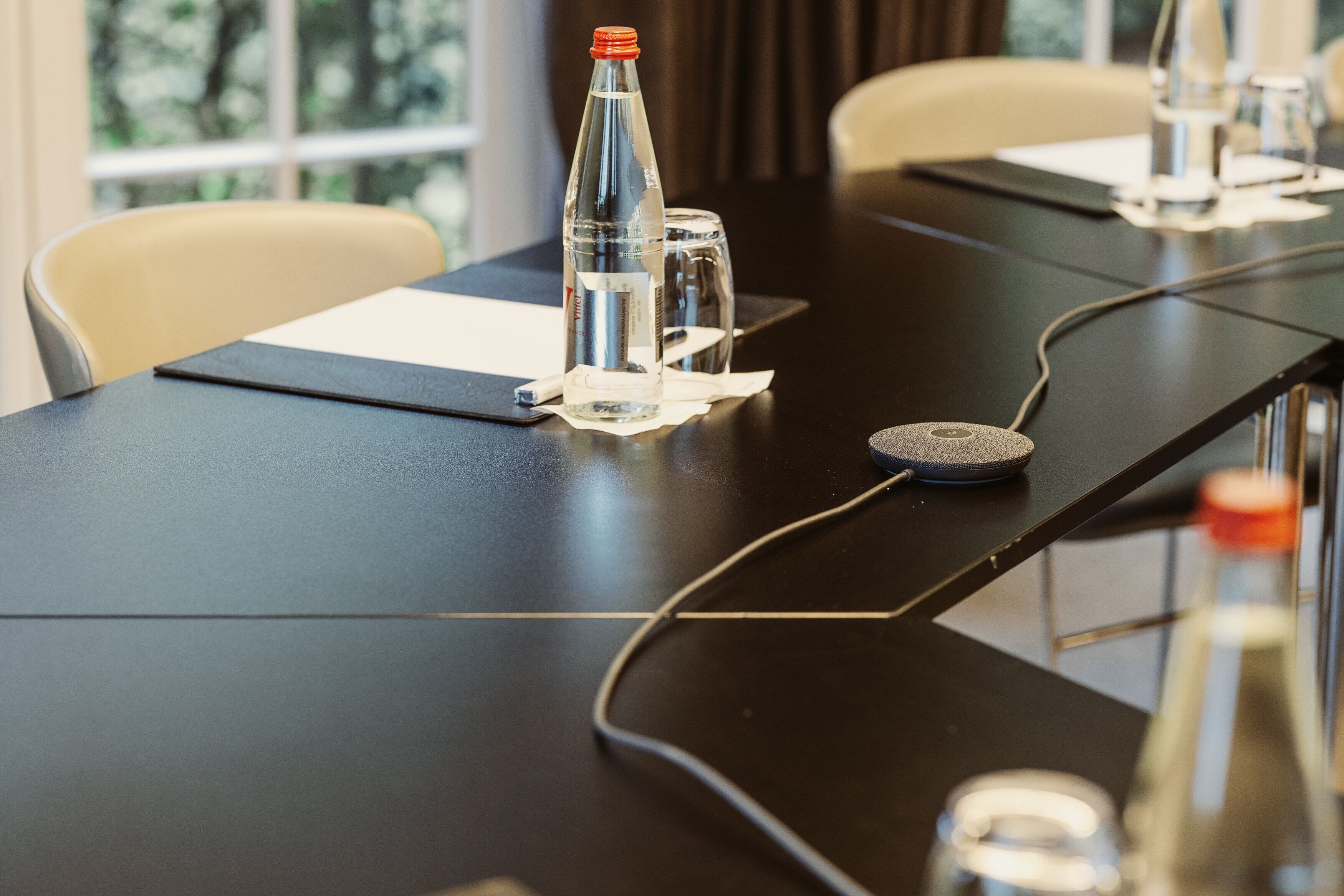 A conference table with a bottle, glass, and a coaster.