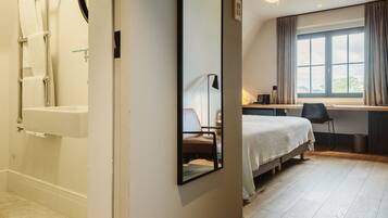 A hotel room with a bathtub, a bed, a desk, and a large window.
