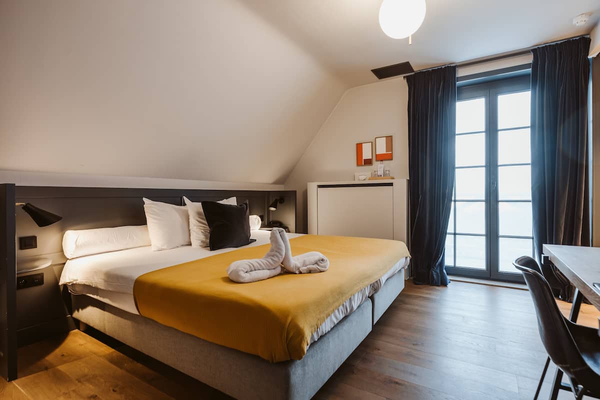 A hotel room with a bed, a desk, and a window with curtains.