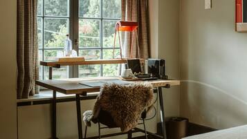 A room with a desk, a chair, a window with curtains, a red lamp, and a small trash bin.