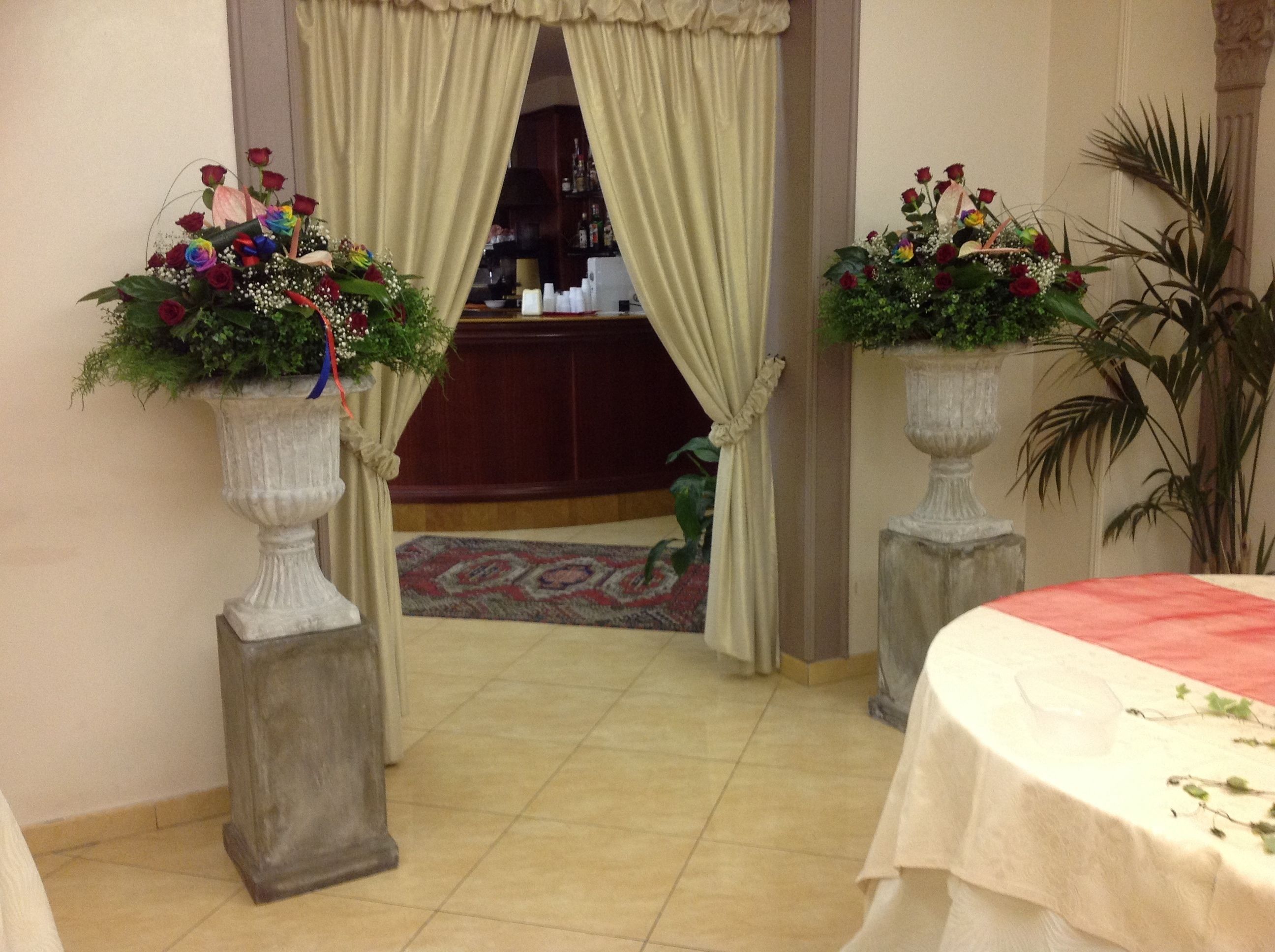 A hotel room with a large bed, a dining table, and two flower arrangements in tall vases.