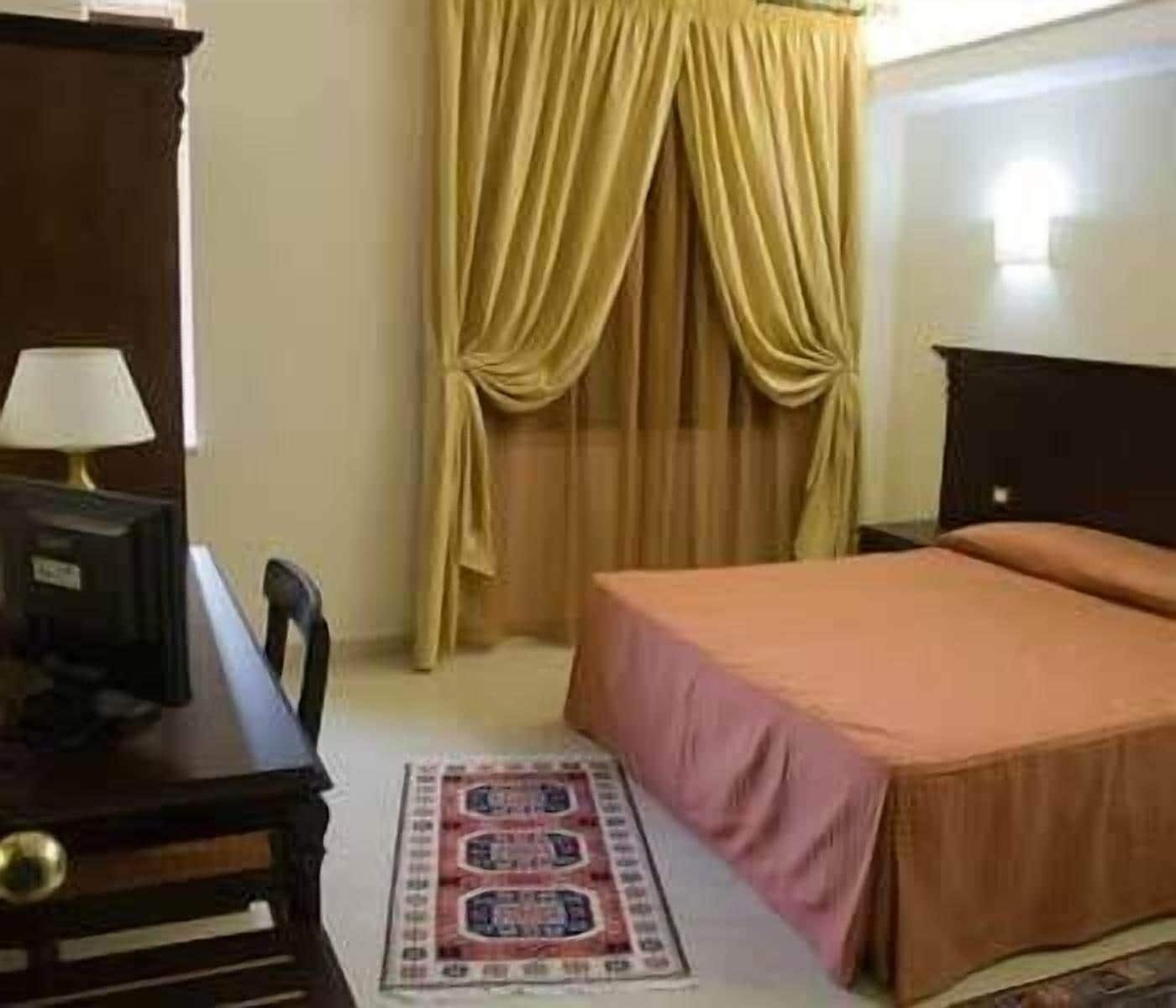 Une chambre d’hôtel avec un lit, un bureau doté d’une lampe et une fenêtre avec des rideaux.