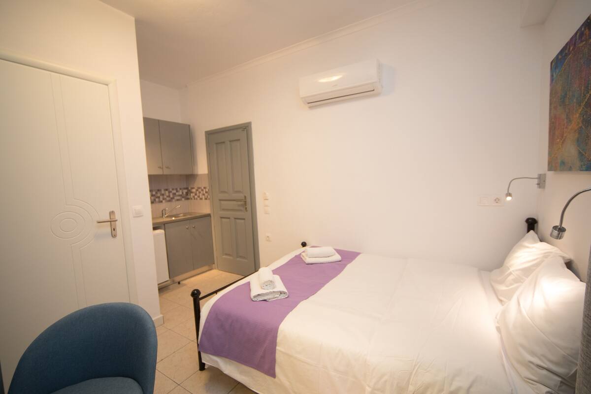 A bedroom with a bed, a chair, a bathroom, and a kitchen.