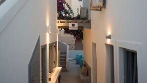 A narrow hallway with a staircase leading to an upper level, a bench, and a small seating area with cushions. - Markakis Studios Fira (Santorini)