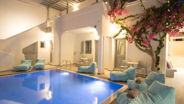 A modern pool area with a blue pool, white walls, and a staircase leading to an upper level. - Markakis Studios Fira (Santorini)