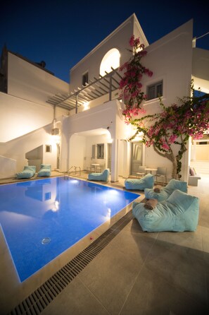 A modern pool area with a blue pool, white walls, and a staircase leading to an upper level. - Markakis Studios Fira (Santorini)