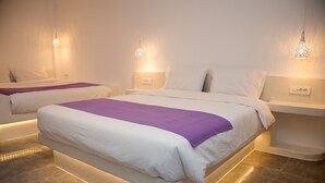 A modern hotel room with a large bed, a smaller bed, and a nightstand with a lamp. - Markakis Studios Fira (Santorini)