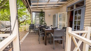 Un patio exterior techado con mesa y sillas, una parrilla y vistas del entorno.