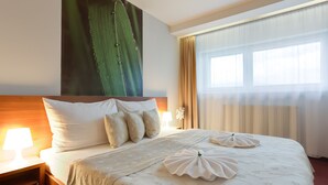 Una habitación de hotel con una cama grande, una mesita de noche con lámpara y una ventana con cortinas.