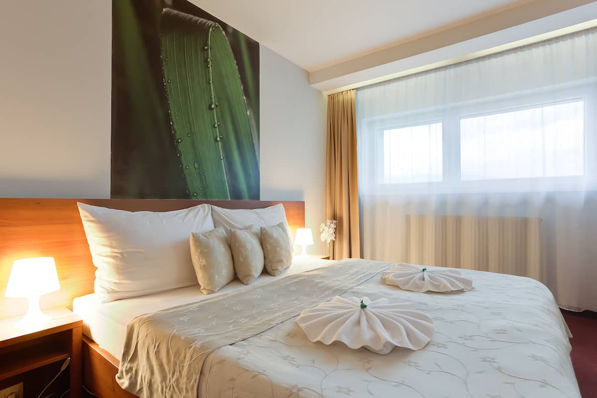 Una habitación de hotel con una cama grande, una mesita de noche con lámpara y una ventana con cortinas.