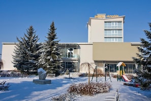 Un hotel llamado "HOTEL JANOŠIK" con un paisaje nevado, un parque infantil y una gran escultura en primer plano.