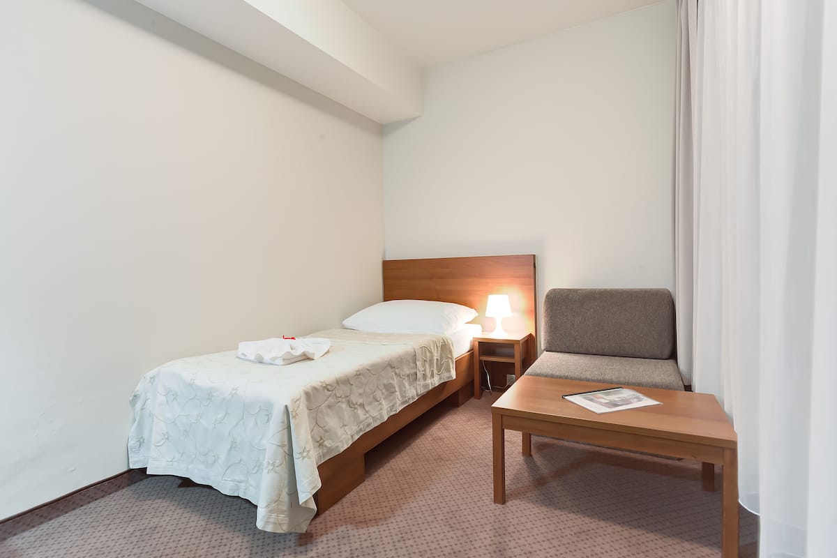Una habitación de hotel con una cama, una mesita de noche con lámpara, una silla y una pequeña mesa.