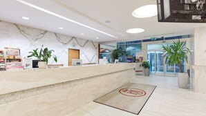 Zona de recepción de un hotel con mostrador de mármol, plantas en macetas y vista despejada a la entrada.