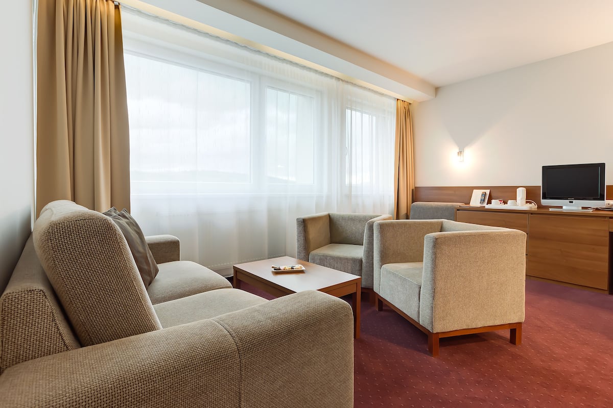 Habitación de hotel con sofá, sillones, una mesita, televisor y escritorio con lámpara.