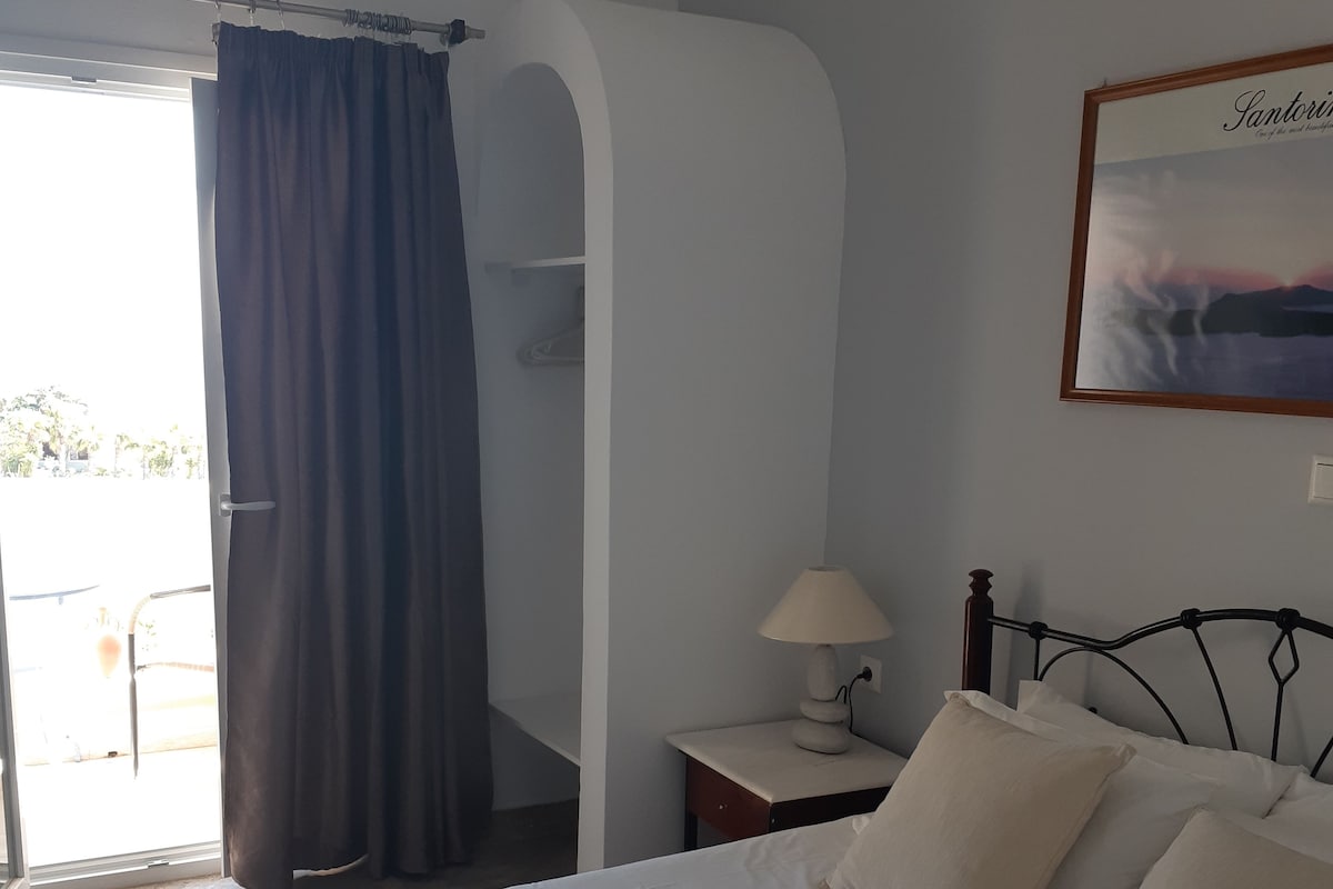 Una habitación de hotel con una cama, una mesita de noche con lámpara, una ventana con cortinas y un aire acondicionado instalado en la pared.