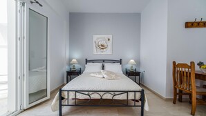 A bedroom with a bed, two bedside tables with lamps, a wooden chair, and a painting on the wall. - Emmanouela Studios (Santorini)