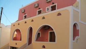 A multi-story building with a distinctive architectural style featuring arched windows and balconies. - Emmanouela Studios (Santorini)