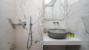 A bathroom with a marble wall, a shower, a sink with a round basin, and a mirror above the sink. - Emmanouela Studios (Santorini)