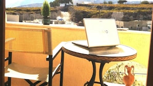 A balcony with a laptop on a small round table, a wicker chair, and a potted plant. - Emmanouela Studios (Santorini)
