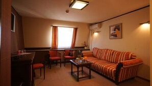 A cozy living room with a striped sofa, a wooden coffee table, and two red chairs. There is a window with curtains, a small table with a plant, and a framed picture on the wall. - Levoslav House Villa (Sibiu)
