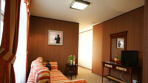 A hotel room with a sofa, a small table with a vase of flowers, a television on a wooden stand, and a framed picture on the wall. - Levoslav House Villa (Sibiu)
