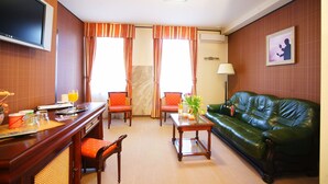 A hotel room with a wooden desk, two chairs, a green leather sofa, a TV, and a painting on the wall. - Levoslav House Villa (Sibiu)
