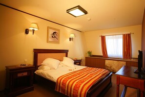 A hotel room with a bed, bedside lamps, a desk, a television, and a window with curtains. - Levoslav House Villa (Sibiu)