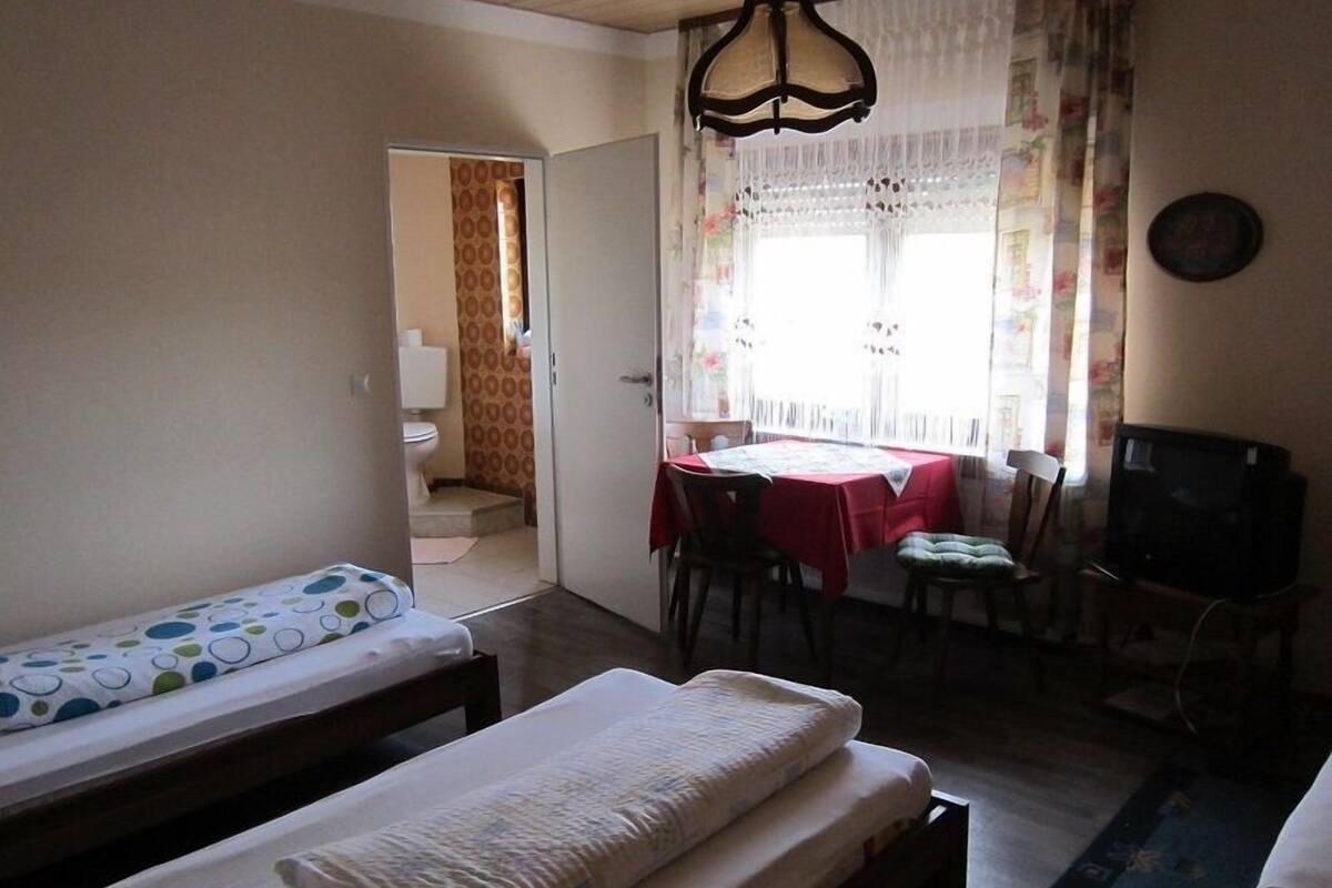 Une chambre avec deux lits simples, une table à manger avec des chaises, un téléviseur et une fenêtre avec des rideaux.