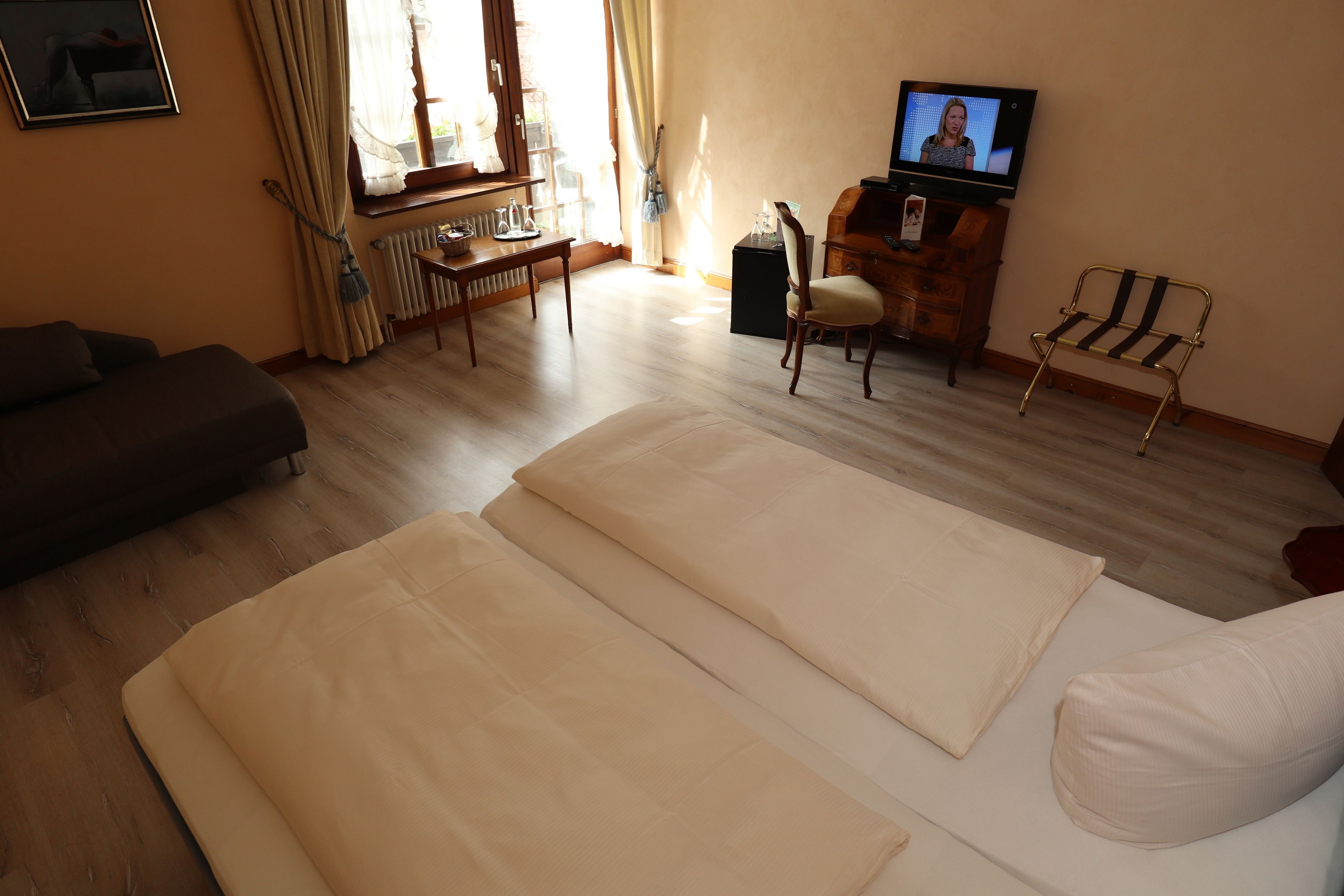 A hotel room with a sofa, a bed with white linens, a wooden desk, a chair, a television, and a radiator.