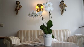 A room with a striped sofa, a round wooden table with a white vase and orchid, and wall-mounted lamps. - Schwarzwaldhotel & Restaurant Stollen (Gutach im Breisgau)