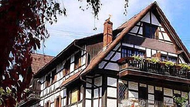 A traditional half-timbered house with multiple stories, large windows, and a balcony with plants. - Schwarzwaldhotel & Restaurant Stollen (Gutach im Breisgau)