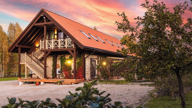 A rustic chalet with a sloped roof, wooden balcony, and a gravel driveway. - Karlamuiza Country Hotel (Cesis Municipality)