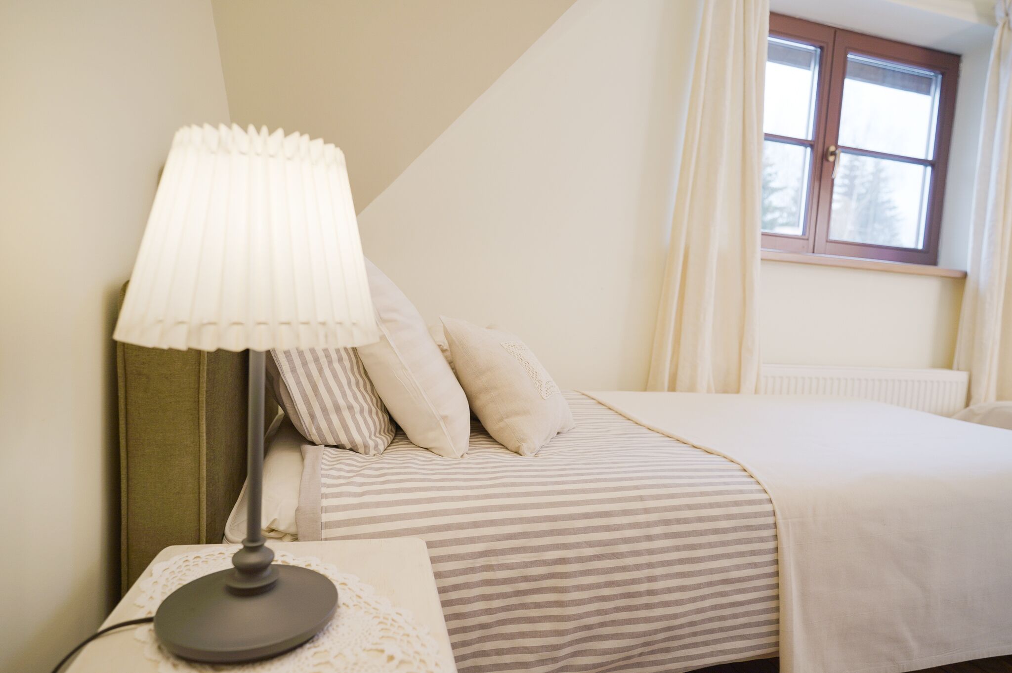 Una camera da letto con un letto, un comodino con una lampada, una finestra con tende e un termosifone.