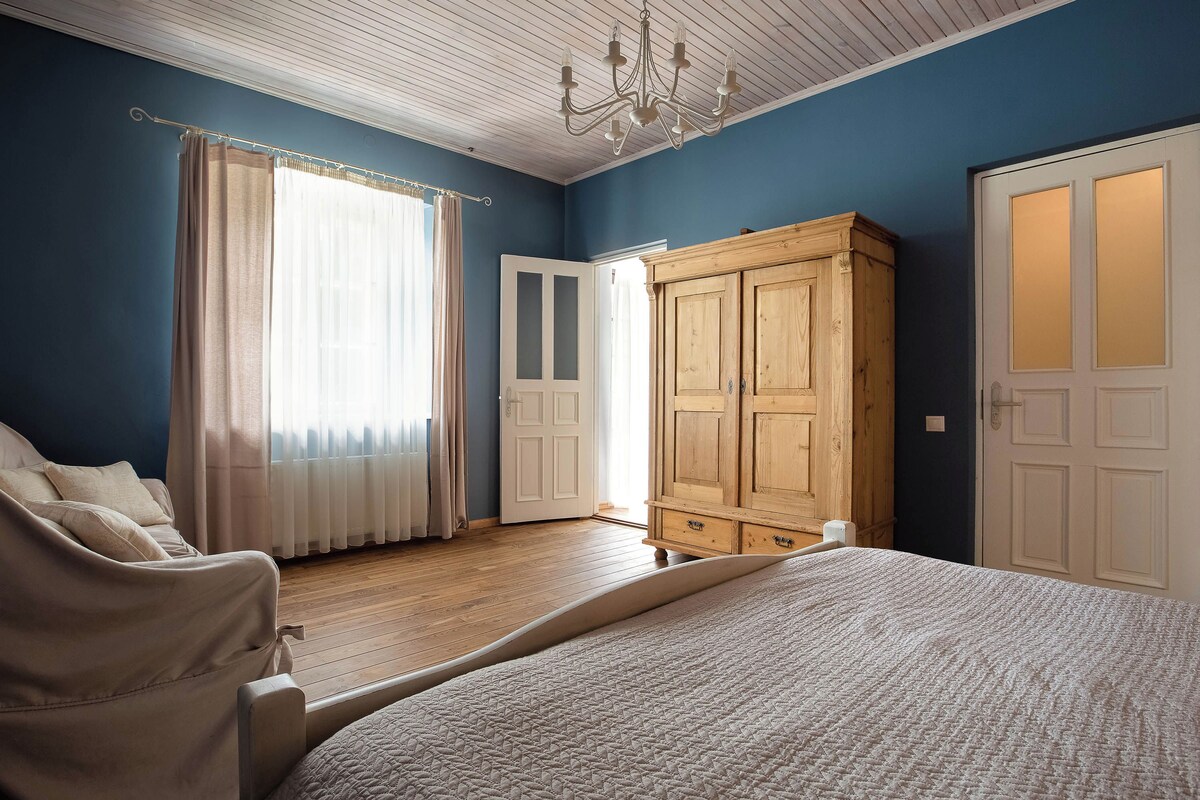 A bedroom with a bed, a wooden wardrobe, a white door, and a window with curtains.