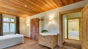 A room with a wooden ceiling, a bed, a wooden dresser, a wall-mounted light, and a view of a bathroom through an open door. - Karlamuiza Country Hotel (Cesis Municipality)