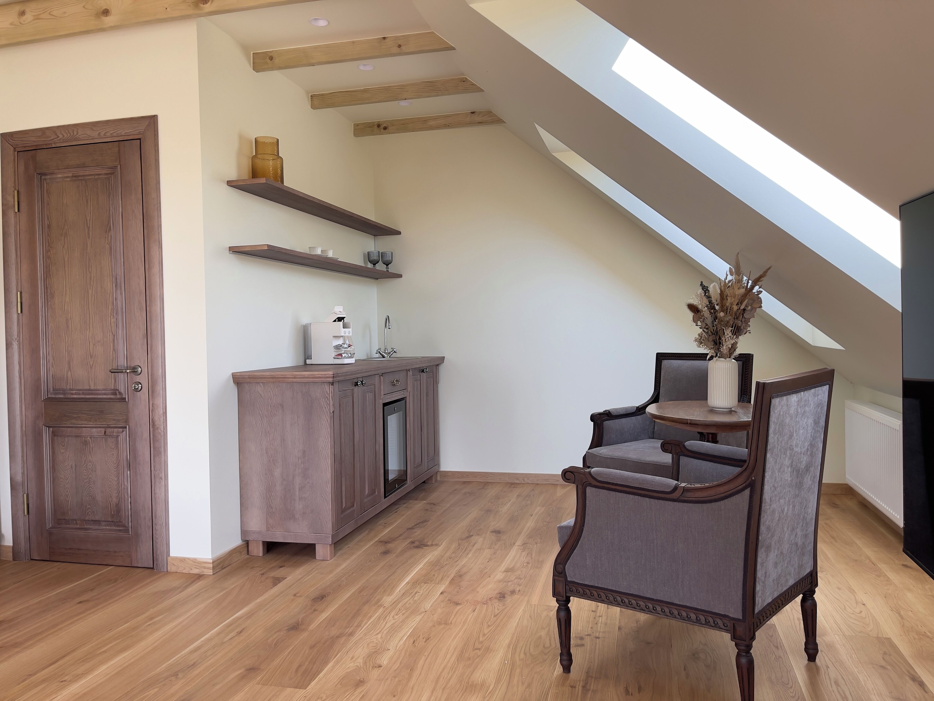 A spacious loft with a high ceiling, wooden beams, a built-in kitchen, and a cozy seating area.