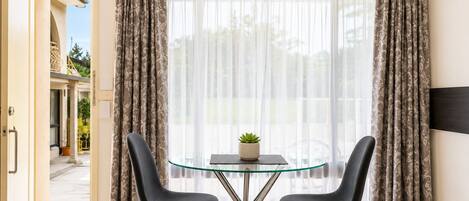 Quarto com uma mesa de vidro, duas cadeiras, uma planta em vaso e cortinas.