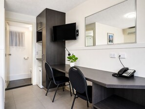 A hotel room with a desk, two chairs, a television mounted on the wall, a telephone, a potted plant, and a mirror. - Gallery Motel (South Murwillumbah)