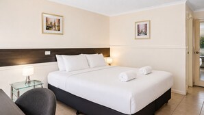 Habitación de hotel con cama, dos lámparas de noche, una silla y dos cuadros en las paredes.