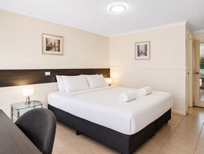Habitación de hotel con cama, dos lámparas de noche, una silla y dos cuadros en las paredes.