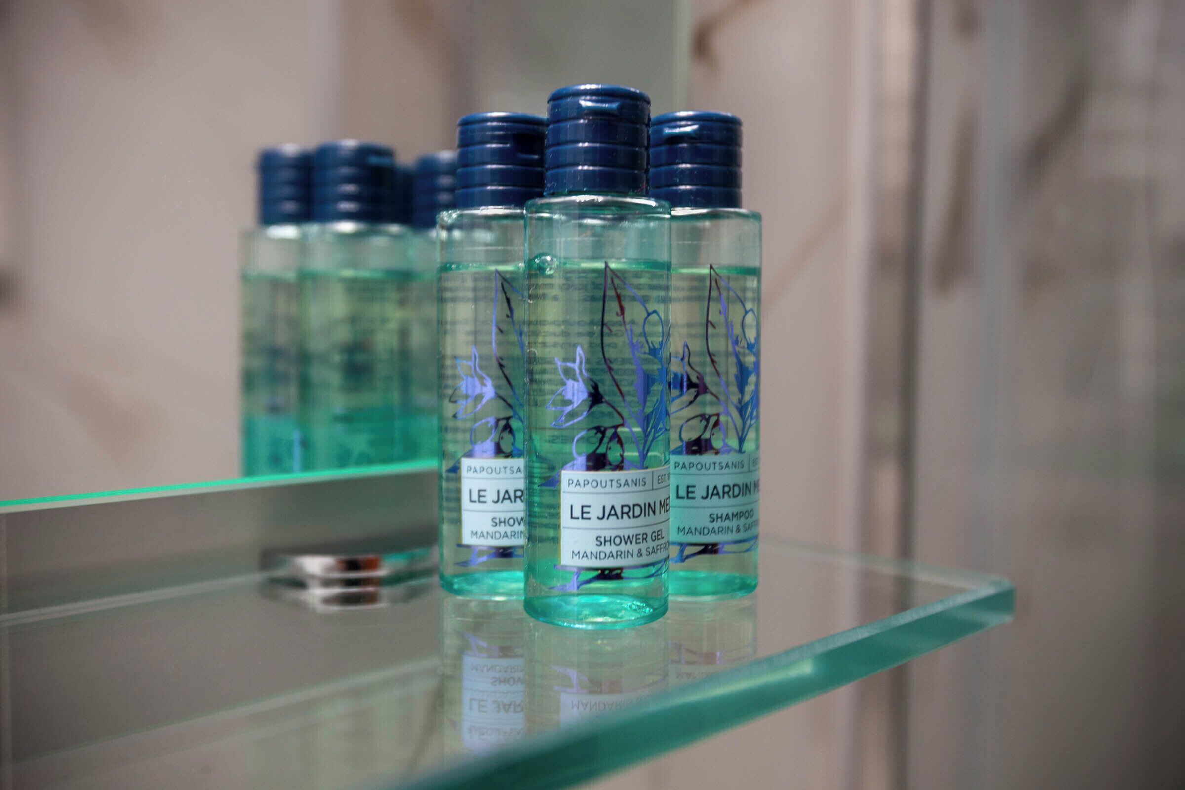 A glass shelf with multiple bottles of shower gel labeled 'Le Jardin'.