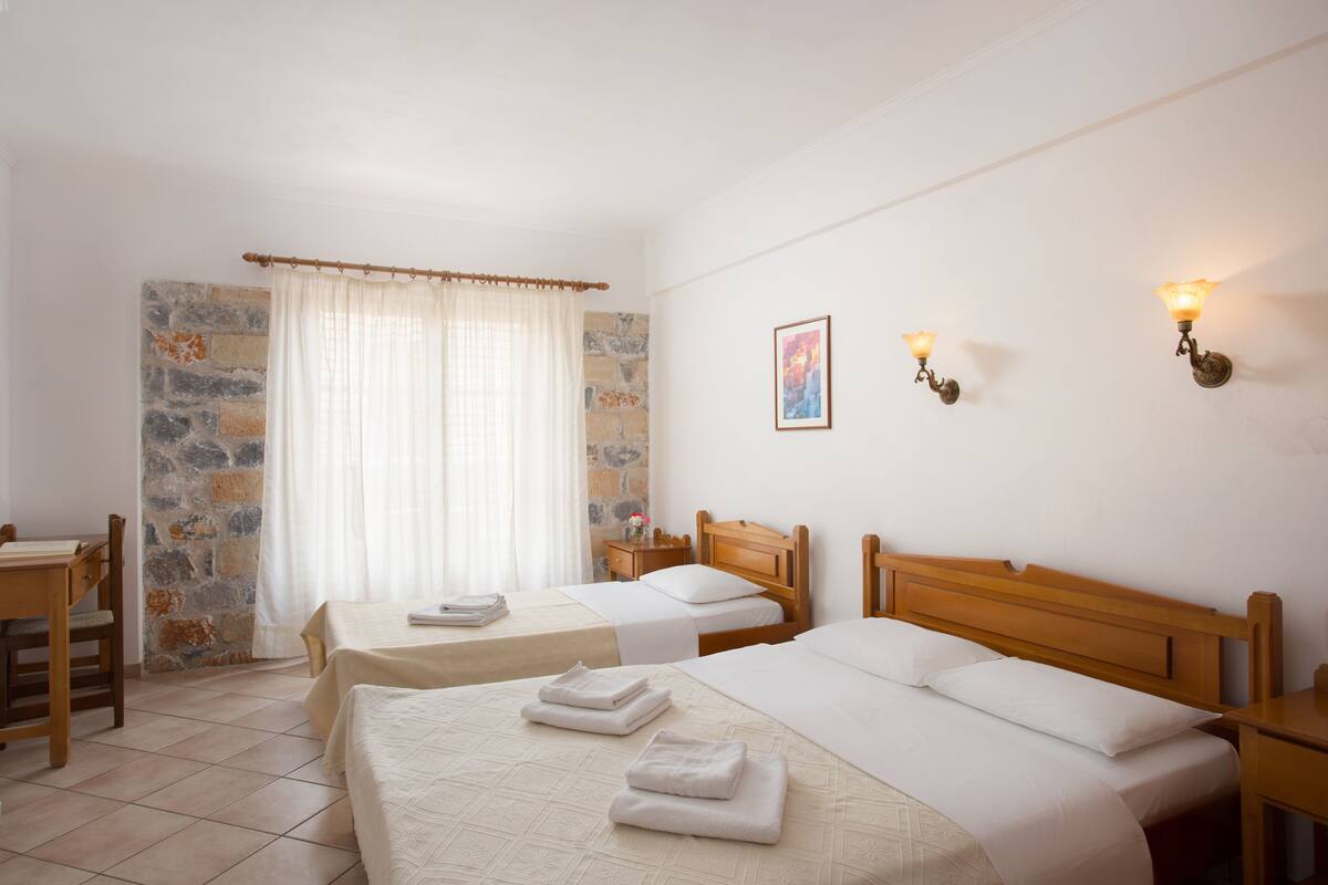 A hotel room with two beds, a stone wall, a wooden desk, and a chair.