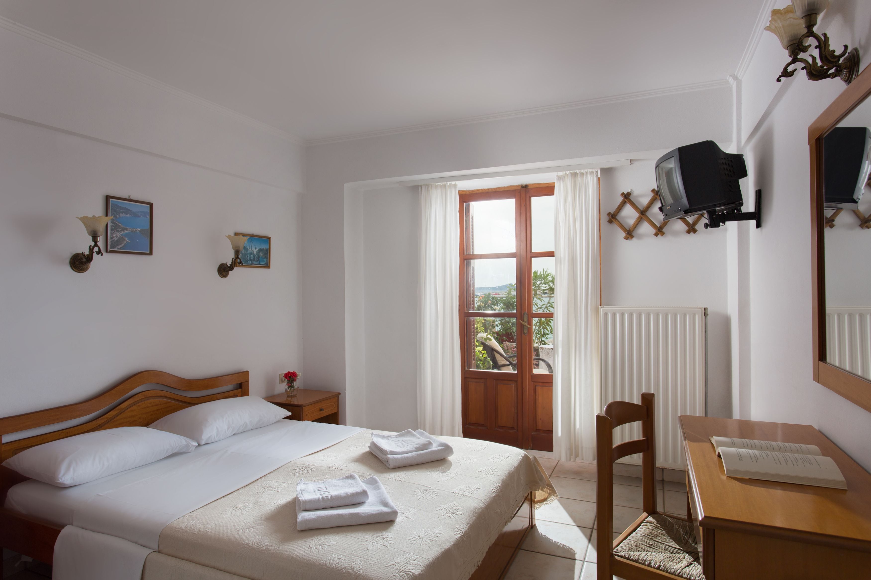 A hotel room with a bed, a desk, a chair, a TV, and a window with curtains.