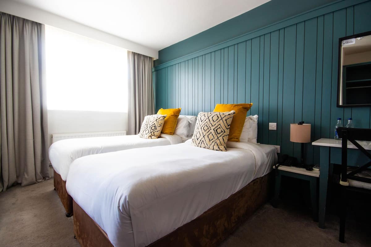 A hotel room with two beds, a nightstand, a lamp, and a mirror on the wall.